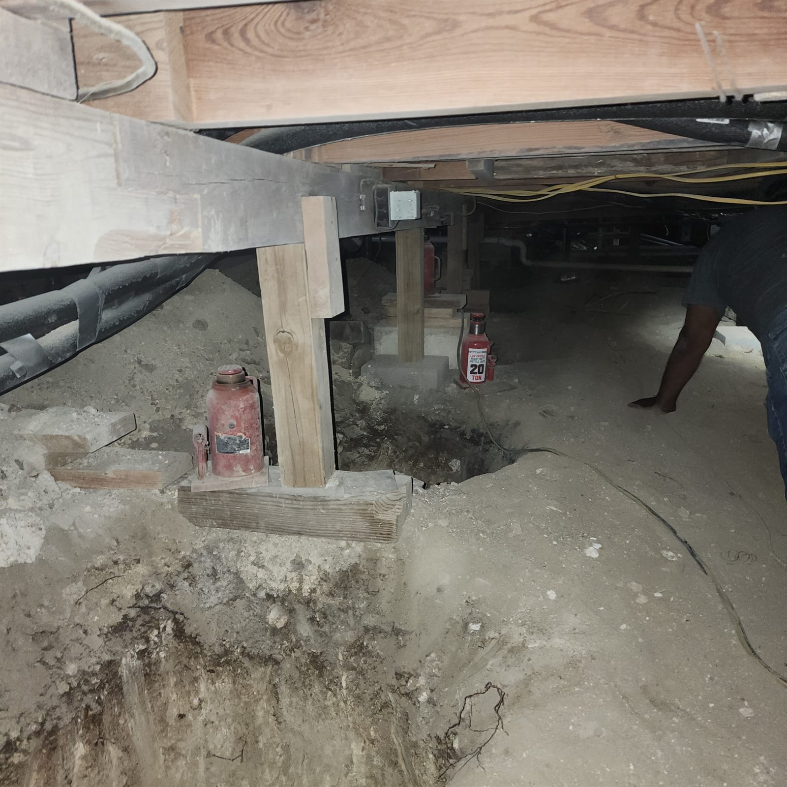 Hydraulic bottle jacks and wood cribbing leveling a beam against a concrete pier